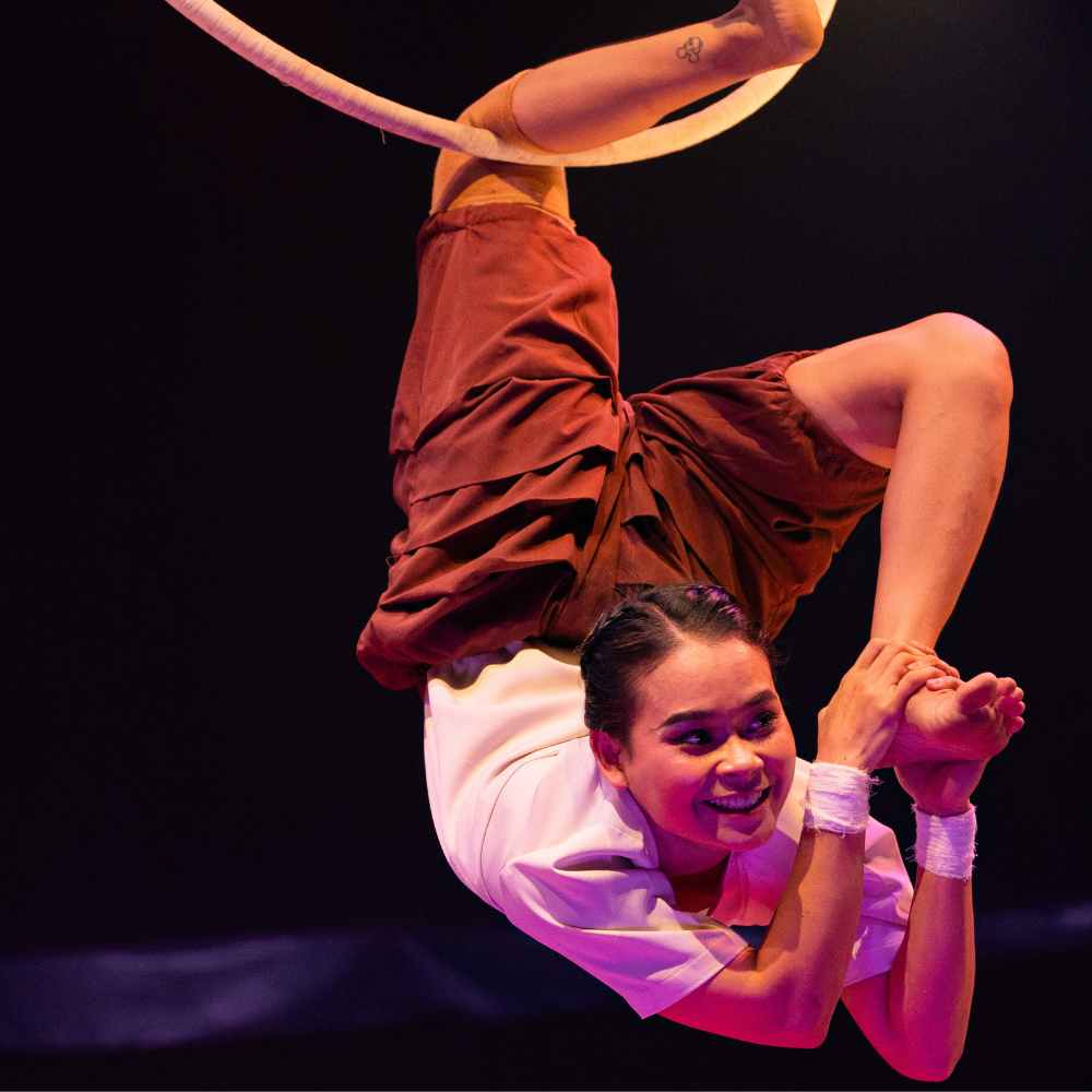 A smiling female acrobat performing an aerial hoop routine during a live Phare Circus show in Siem Reap.