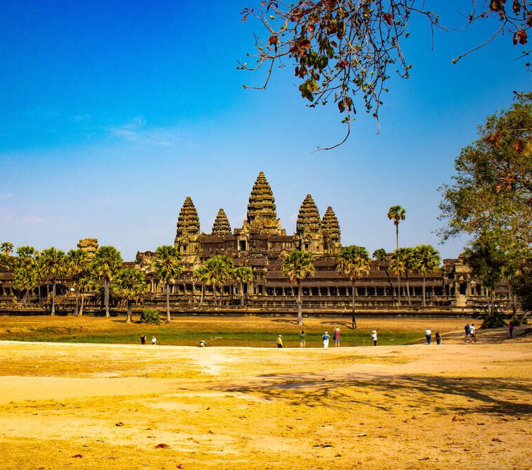 A wide landscape view of the ancient stone towers of Angkor Wat temple under a clear blue sky in Siem Reap.