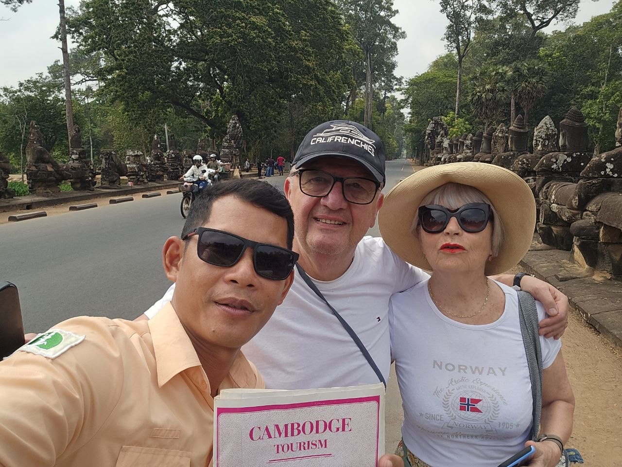 A local Cambodian tour guide taking a selfie with a couple of senior tourists on the South Gate bridge of Angkor Thom in Siem Reap.