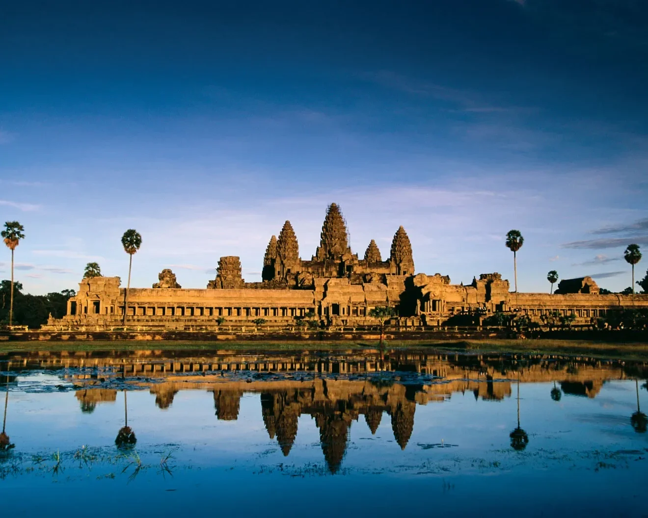 Panoramic view of Angkor Wat temple towers reflecting perfectly in the surrounding lily pond under a blue sky in Siem Reap Cambodia