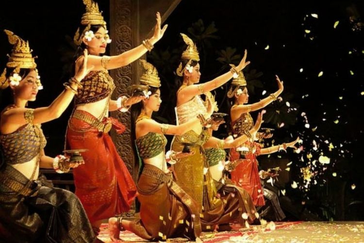 A group of Cambodian Apsara dancers performing on stage in traditional silk dresses and golden headdresses in Siem Reap.