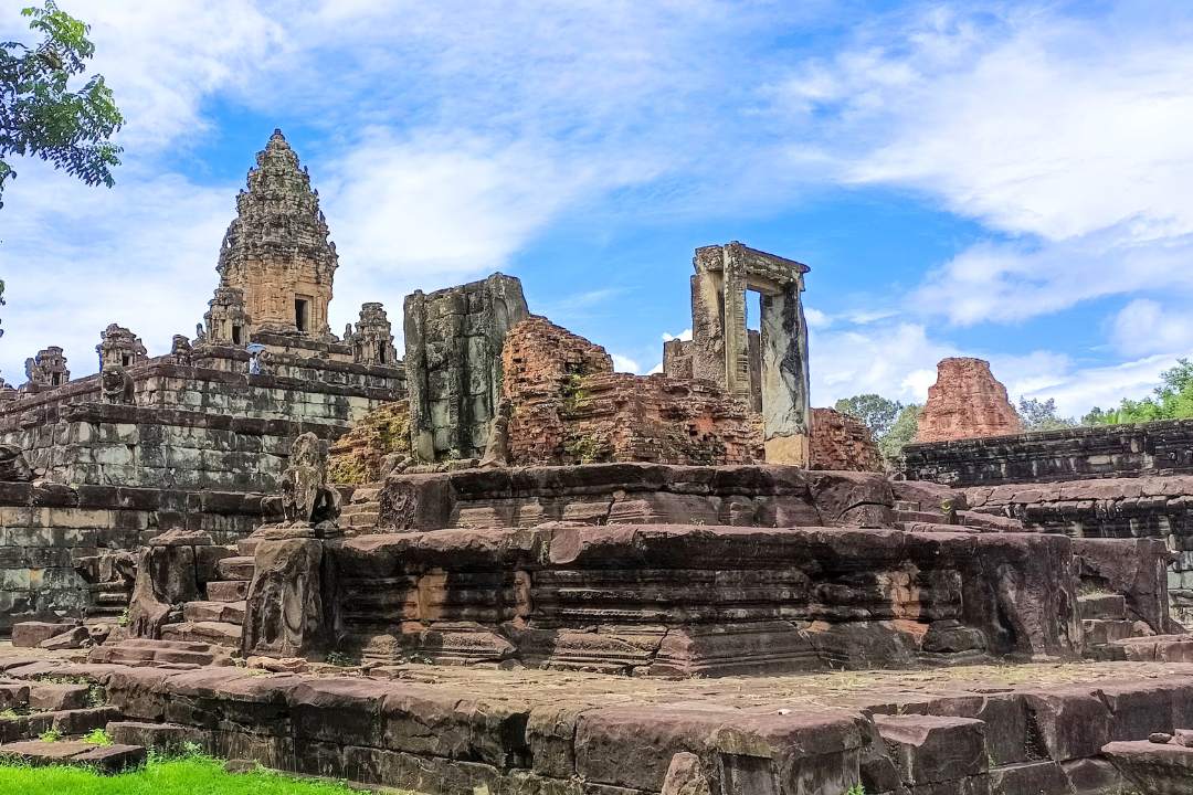 Ancient stone towers and ruined sandstone structures of Bakong temple under a blue sky in Siem Reap Cambodia