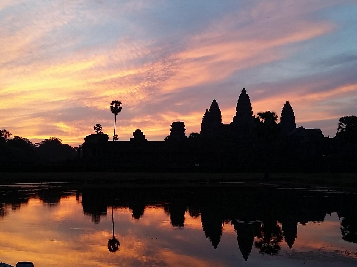 Silhouette of Angkor Wat temple towers reflected in the reflection pond during a vibrant sunrise in Siem Reap.