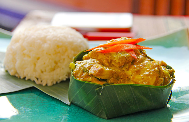 Traditional Cambodian fish amok served in a banana leaf bowl next to a mound of steamed white rice.