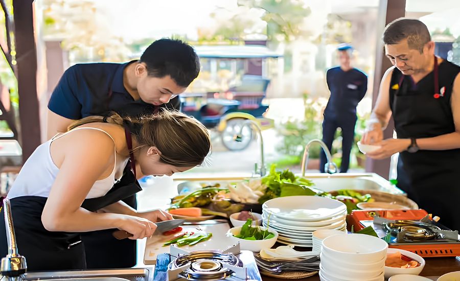 A local chef guiding a student on slicing fresh ingredients at an outdoor cooking station in Siem Reap.