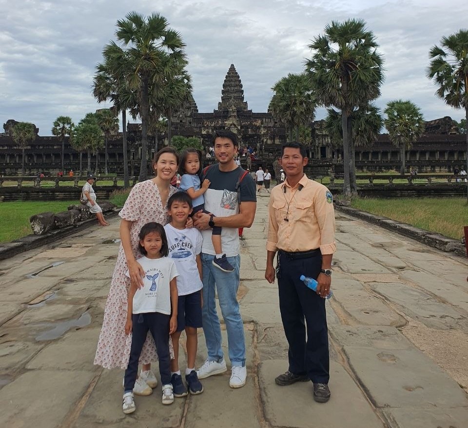 A family with three children posing on a stone causeway with a local guide in front of Angkor Wat temple in Siem Reap Cambodia