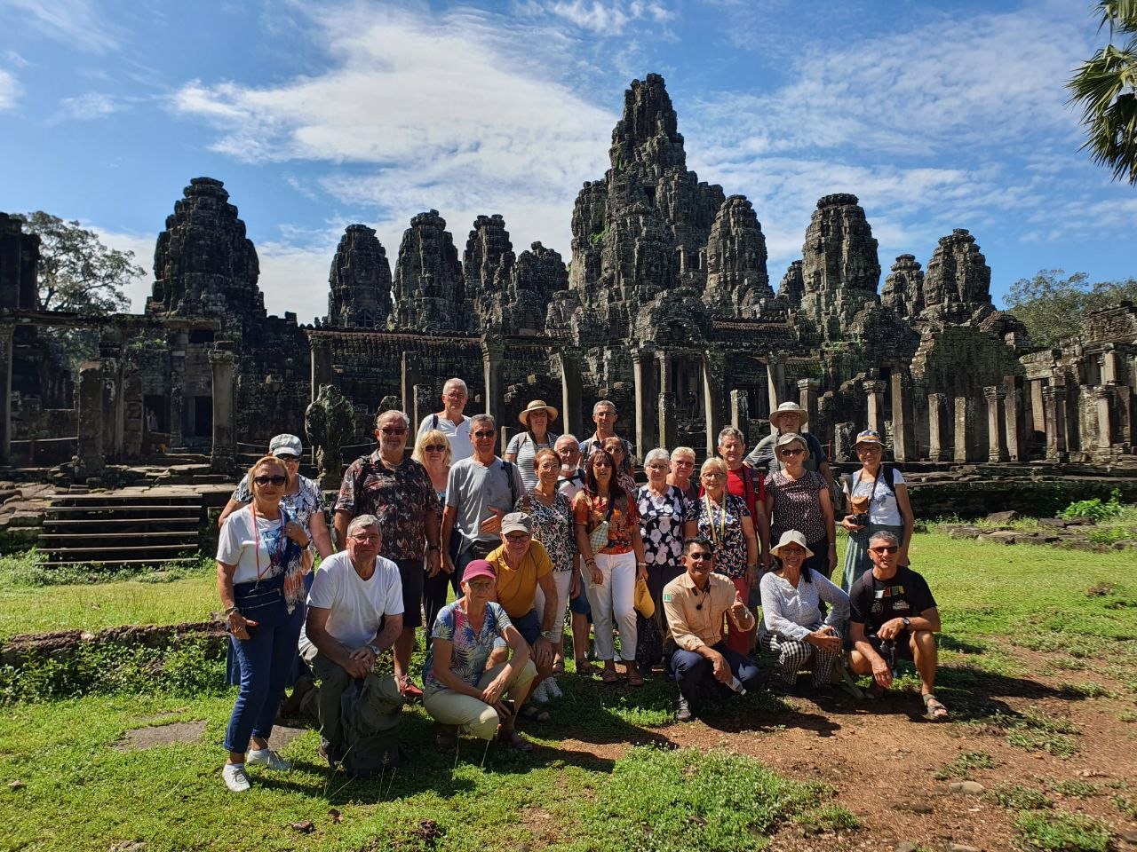 Large tour group posing for a picture in front of the carved face towers at Bayon temple in Angkor Thom