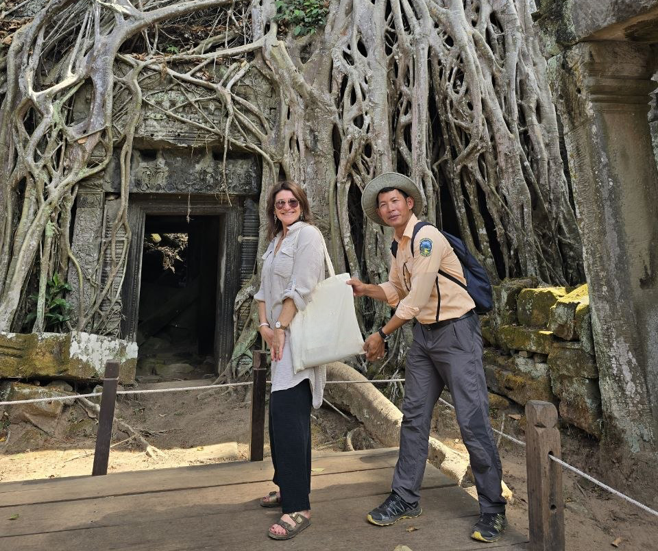 A female tourist and a local guide posing in front of tree roots over stone ruins at Ta Som temple in Siem Reap