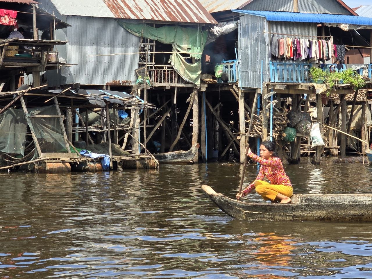A local woman paddling a small wooden boat in front of stilt houses at Kampong Phluk floating village on Tonle Sap Lake near Siem Reap