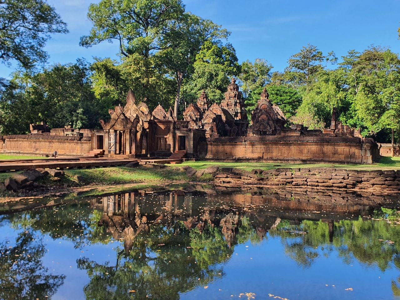 Banteay Srei temple complex reflecting in a calm water moat framed by green trees
