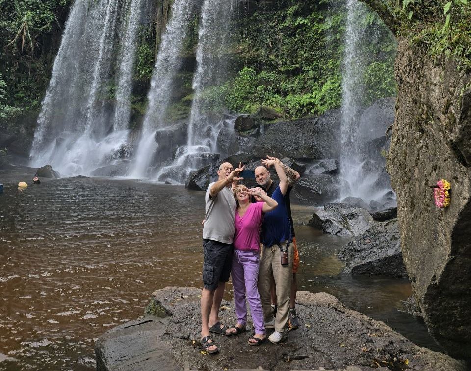 Group of friends taking a selfie on a rock in front of a wide cascading waterfall at Phnom Kulen National Park