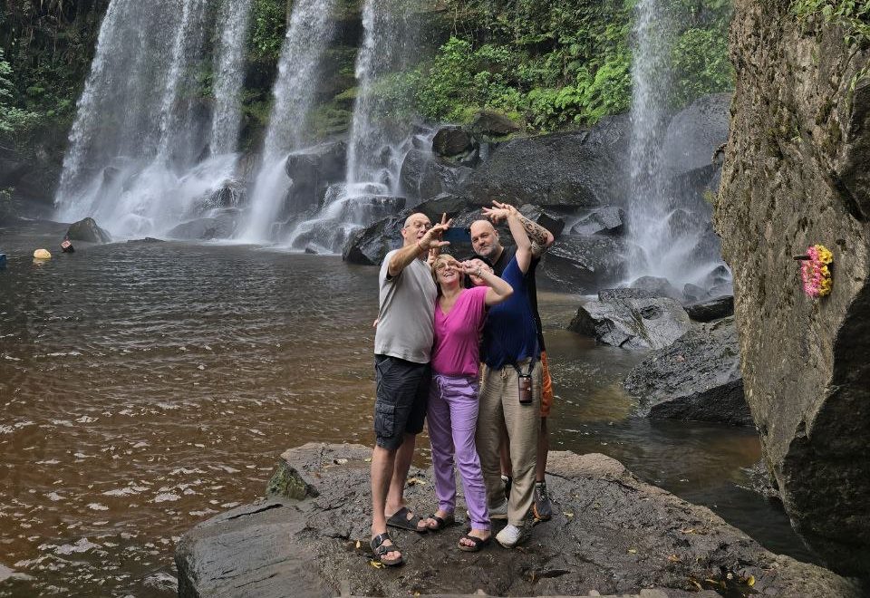 Group of tourists taking a photo in front of a cascading tropical waterfall at Phnom Kulen National Park