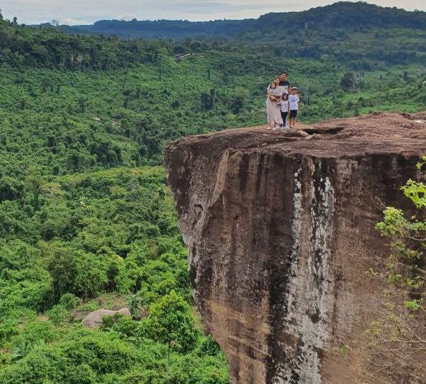 Family standing on a high cliff edge looking out over a vast green jungle canopy at Peung Ta Kho in Phnom Kulen