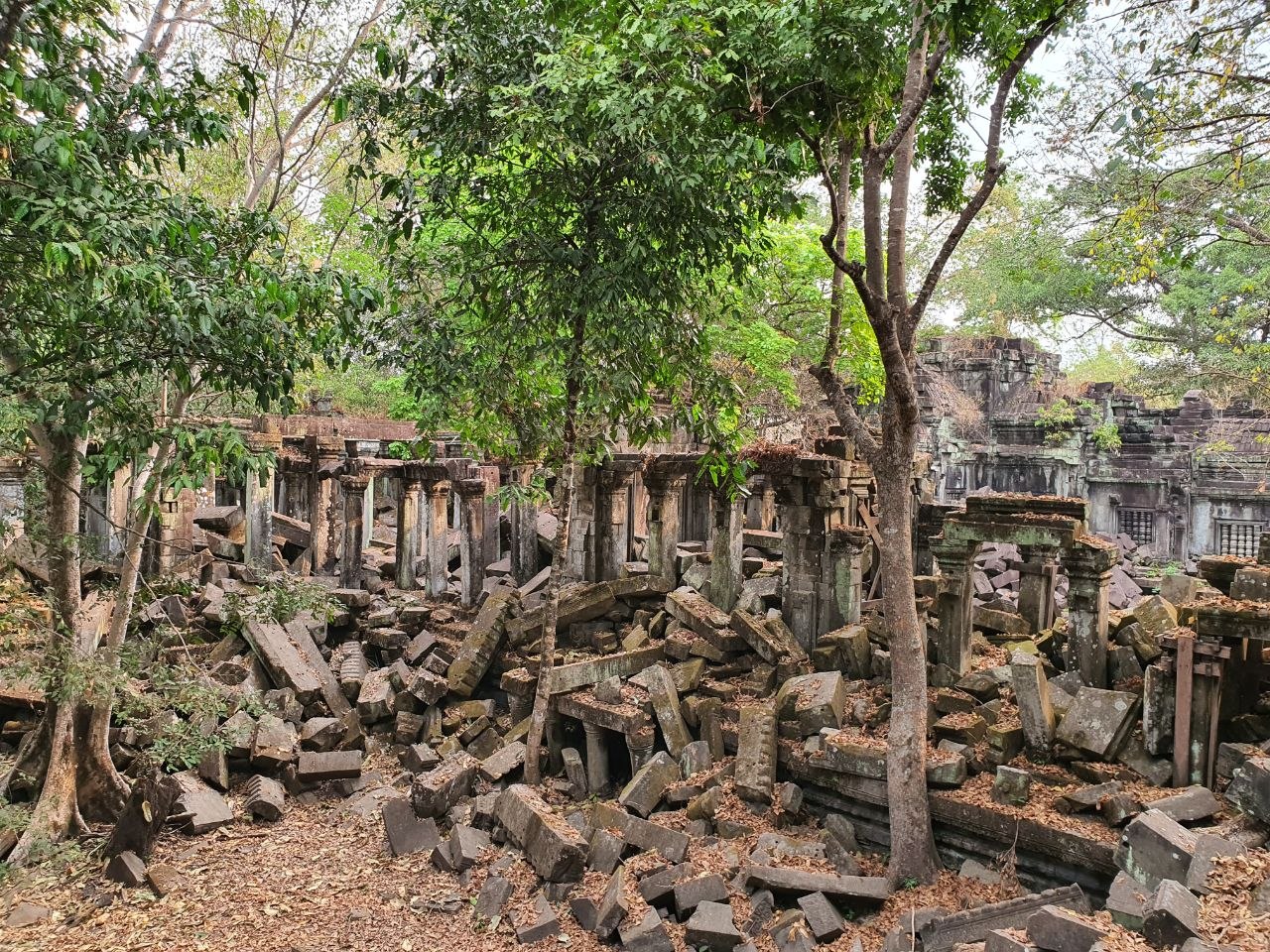 Collapsed stone blocks and standing pillars of Beng Mealea jungle temple surrounded by green forest in Siem Reap