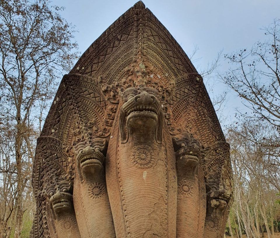 Detailed carved stone five-headed Naga serpent statue standing against a forest background in Cambodia