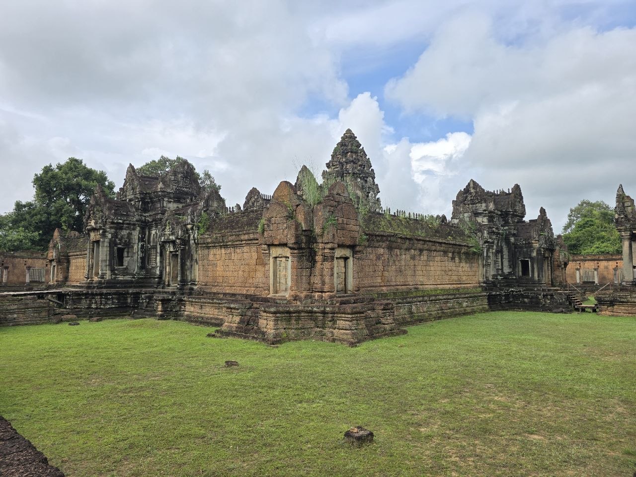 Outer stone walls and carved central tower of Banteay Samre temple surrounded by green grass