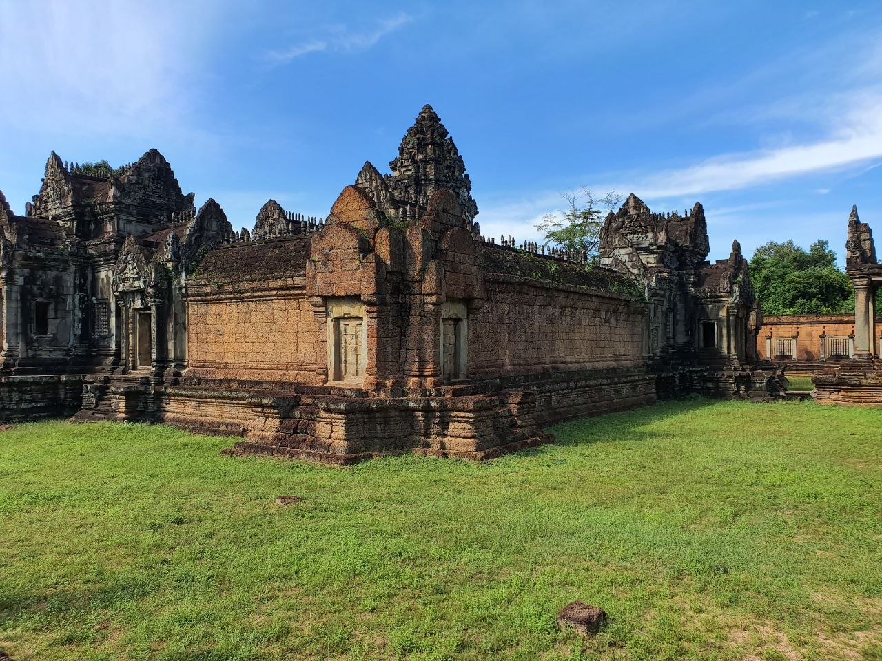 Outer stone walls and carved central tower of Banteay Samre temple surrounded by green grass