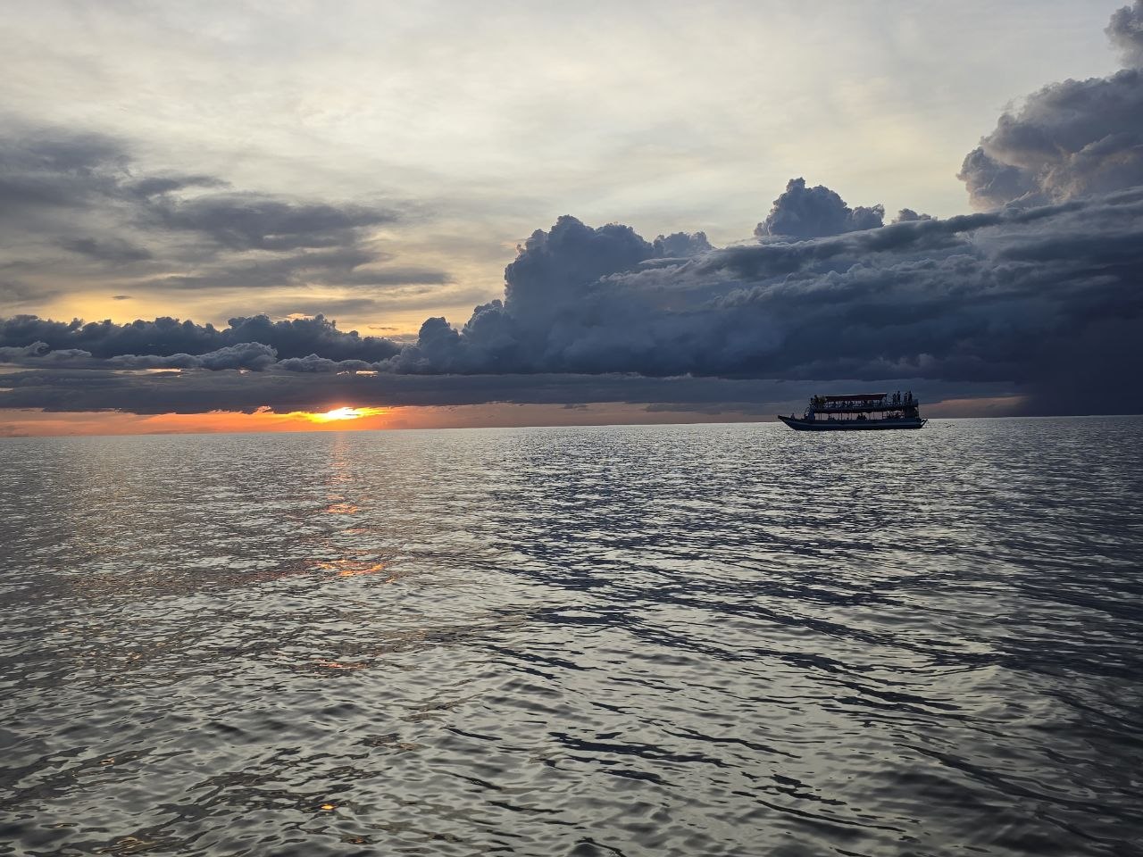 Tourist boat cruising on calm open water during a dramatic orange sunset on Tonle Sap Lake in Cambodia
