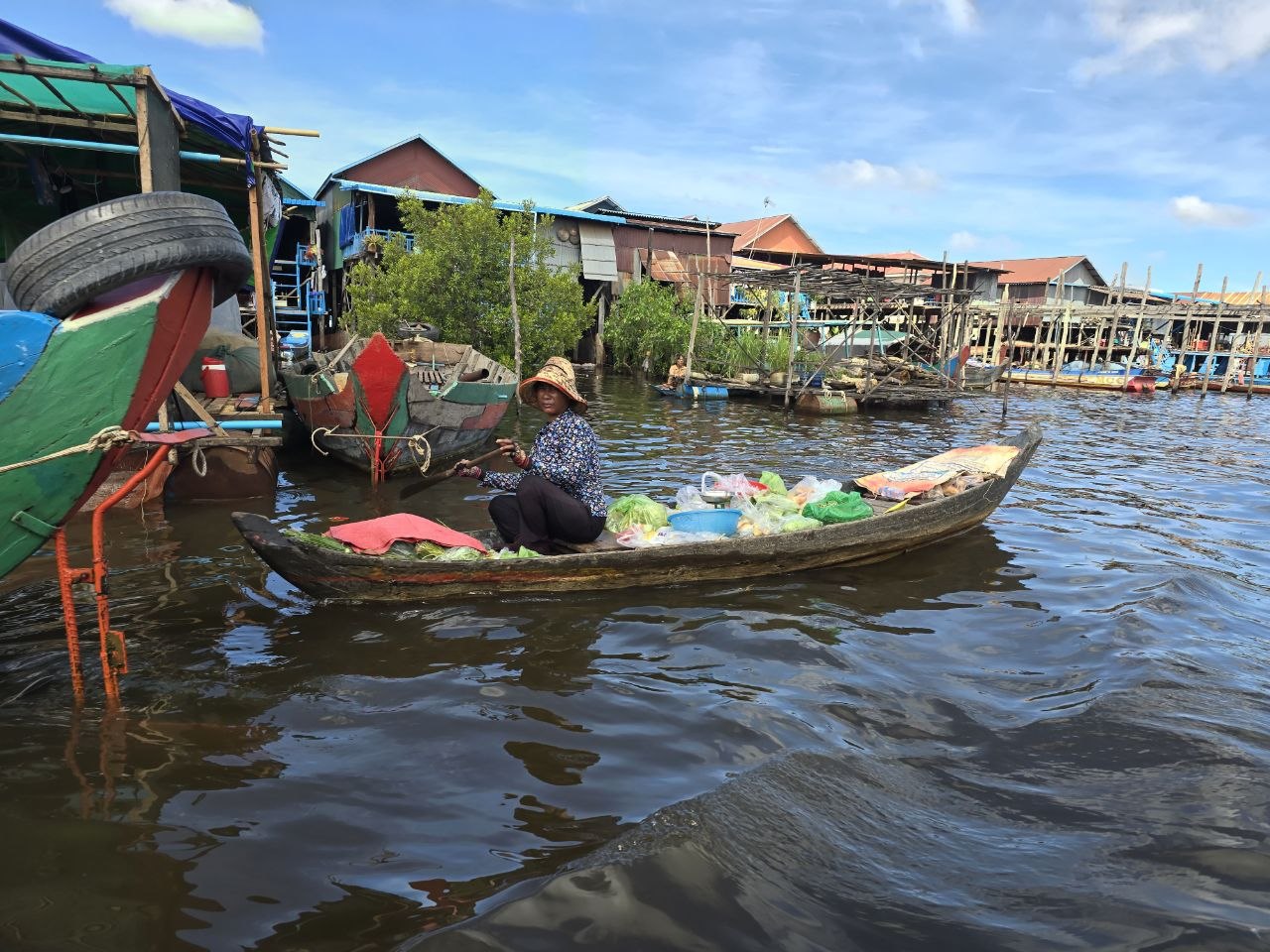 Local vendor paddling a wooden boat filled with fresh vegetables through a floating village on Tonle Sap Lake
