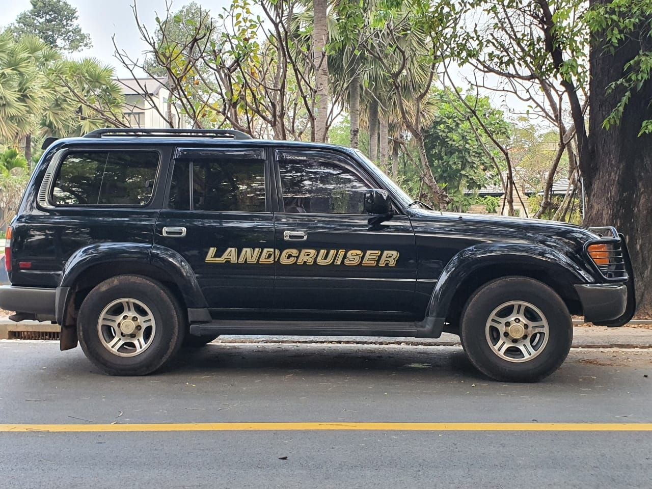 Black Toyota Land Cruiser 80 series SUV parked along a tree-lined street in Siem Reap