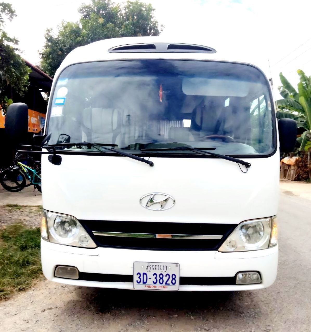 Front view of a clean white Hyundai County tourist minibus parked outdoors in Siem Reap