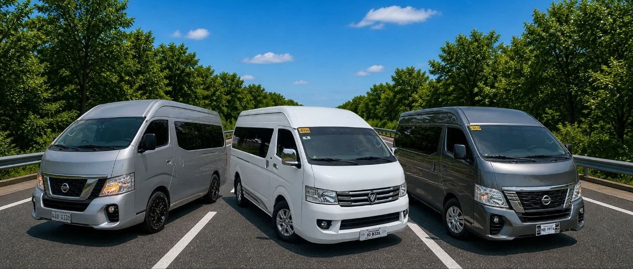 Three modern passenger vans in silver, white, and dark grey parked lined up on a scenic road
